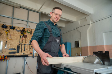 Fototapeta na wymiar The carpenter cuts a wooden board on a circular machine.