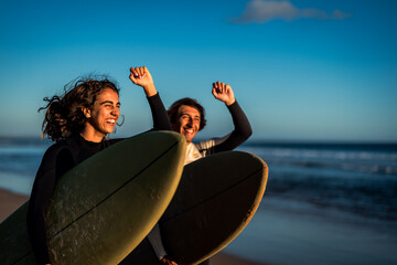 Two surfers prepares to hit the waves as they walking on the beach with their surfboards.