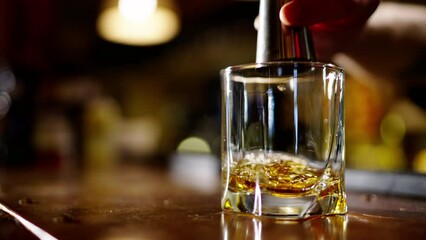 A professional bartender is preparing an alcoholic cocktail with ice cubes to customers at the bar or disco club. Close up of a professional bartender is mixing an alcoholic cocktail with professional