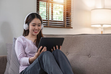 Young asian woman relaxes at home with music on digital tablet