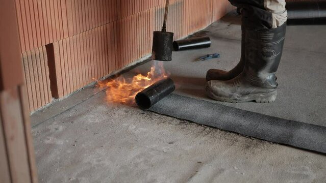 Burning tar bitumen floors to waterproof floor and roof, flaming sheet layers with propane gas burner blowtorch, isolation on production site.