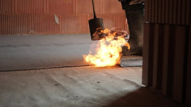 Contractor Worker Flaming Roofing hydro insulation sheet layer Felt with a Propane Gas Burner Welding Torch Bitumen at construction site. Burns it with a flaming blowtorch.