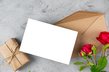 Wedding invitation. Blank greeting card with red rose flowers and gift box on gray background. Mock up. Flat lay.