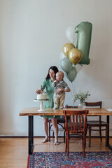 the first birthday of the child, mother and baby stand near the cake and balloons, look and smile