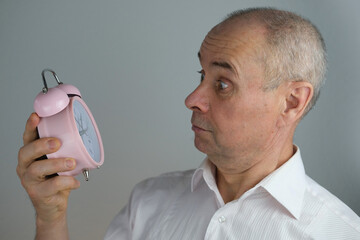 close-up mature man, senior 60 years old holds alarm clock in hand, concept missing time,...