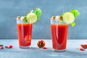 Bloody Mary cocktail with garnish and ice on a blue background. Spicy tomato juice with alcohol, lime, pickles, celery, and peppers