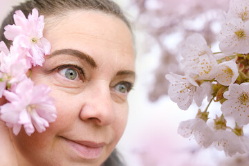 close up part of female face in flowers, beautiful woman 50 years old, human eyes looking to side,...