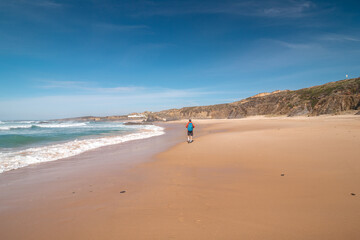 Fototapeta na wymiar Backpacker walks along Praia do Almograve with a smile on his face. The joy of moving and discovering new places. Odemira region, western Portugal. Wandering along the Fisherman Trail, Rota Vicentina