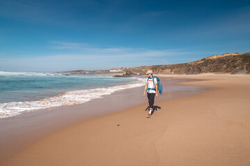 Backpacker walks along Praia do Almograve with a smile on his face. The joy of moving and discovering new places. Odemira region, western Portugal. Wandering along the Fisherman Trail, Rota Vicentina