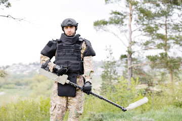 A man in a military uniform and bulletproof vest works in the forest with a metal detector. A minesweeper performs work on demining the territory