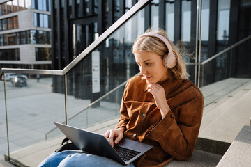 Woman in headphones working on laptop while sitting on stairs outdoors