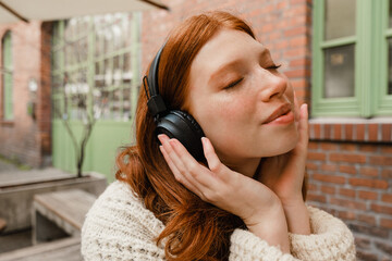 Young girl listening music with headphones while sitting outdoors