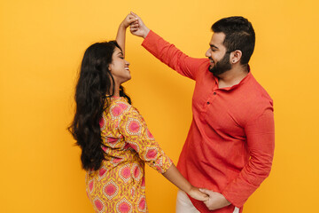Indian man and woman holding hands and dancing isolated over yellow background