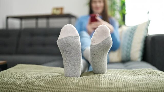 Young caucasian woman using smartphone moving foot at home