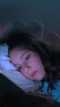 Teen girl lying in bed at night using smartphone, scrolling social media and texting. Not healthy sleep. Insomnia and the harm of the smartphone before going to bed. Dependence on social networks