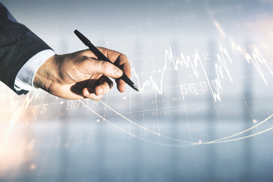 Multi exposure of trader hand with pen working with virtual abstract financial graph interface on blurred office background, financial and trading concept