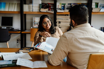 Smiling indian woman student talking with сollege classmate while studying in library