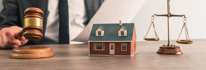 The hand of a judge with a gavel and a model of a house mediating property disputes in court