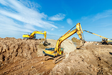 Two Excavator are digging soil in the construction site on sky background,with white fluffy cloud