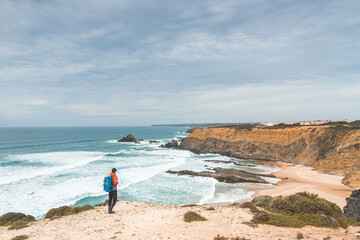 Backpacker enjoys his hike along the Fisherman Trail, Portugal. View of Alteirinhos Beach near Zambujeira do Mar, Odemira region. Atlantic Ocean, rocky cliffs and beach