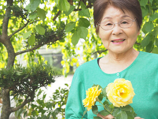 庭で育てた黄色いバラを持つ笑顔の高齢女性
