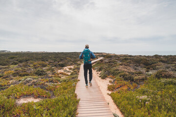 Young and courageous Vagabund roaming the Portuguese countryside. A backpacker walks along a wooden walkway in the Odemira region of Portugal. Fisherman Trail, Rota Vicentina