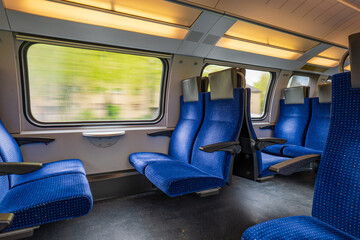 Fototapeta premium Passenger train with empty seats. Wide-angle long exposure, blurry green background out the window of an empty train in Switzerland, Europe, no people