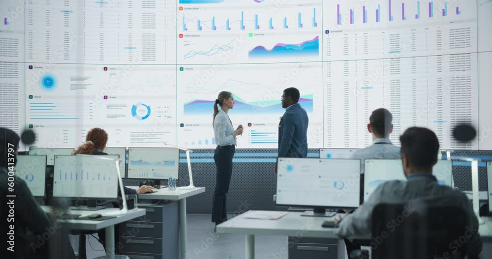 Aufkleber Black Male Data Scientist And Caucasian Female Project Manager Having A Meeting In Monitoring Office With Analytics Feed On Big Digital Screen. Big Data Company With Employees Behind Computers