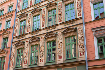 Fototapeta na wymiar Facade of an ancient architectural building with pink walls, tall windows in green frames and decorative elements. Historical architecture. Old town. Poland, Wroclaw, January 2023.