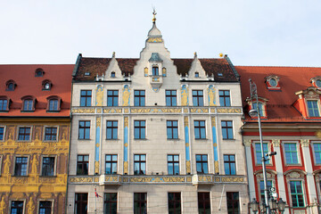Facade of an ancient architectural buildings with white, red and yellow walls, tall windows, decorative elements and red roofs. Historical architecture. Old town. Poland, Wroclaw, January 2023.