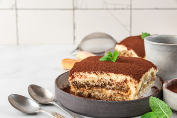 Italian homemade tiramisu cake with fresh mint on plate and coffee cup and spoons on white background