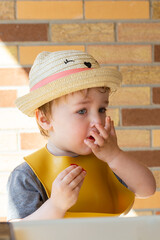 Selective focus vertical view of fair toddler boy sitting in high chair on terrace stuffing his...