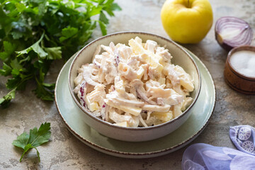 Light breakfast: salad with squid, fresh vegetables and fresh parsley, seasoned with mayonnaise, on a beautiful plate on a gray background. Close-up.