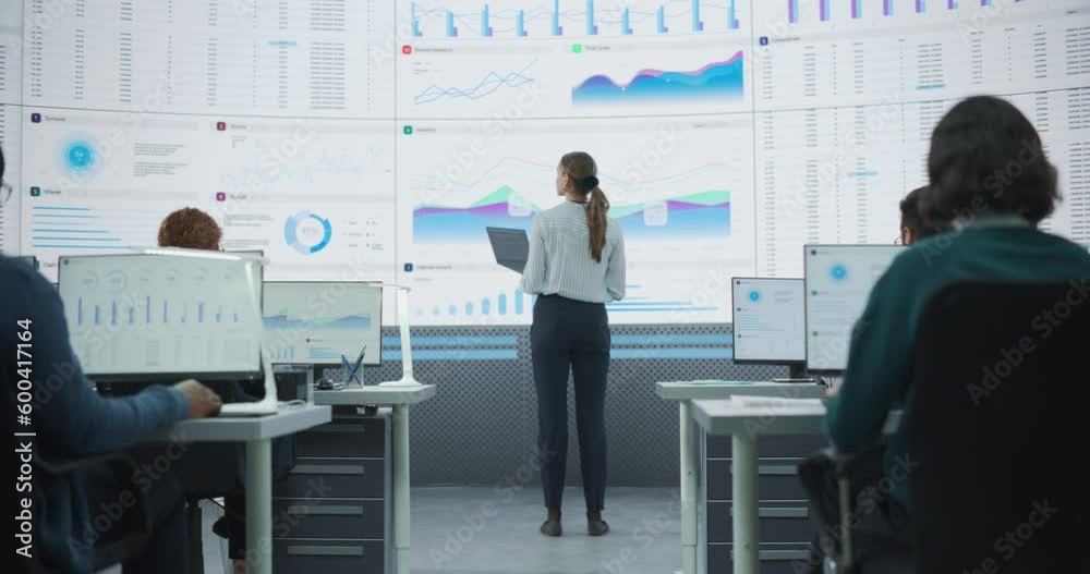 Poster Zoom Out Back View Shot Of Female Data Scientist Using Laptop And Analyzing Information On Big Digital Screen in Monitoring Office. Diverse Employees Working On Desktop Computers For Big Data Company