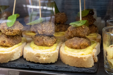 A typical tapa or aperitif served in a Spanish bar, two meatballs with peppers on bread spread with cheese.