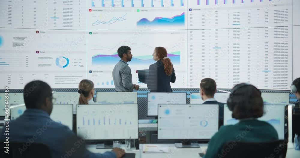 Poster Wide Shot of Diverse Male And Female Data Analysts Discussing Graphs And Reports On Big Digital Screen In Monitoring Office. Multiethnic Employees Working On Desktop Computers And Listening to Music.