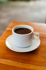 Fototapeta premium Black hot Americano in a white mug on a wooden table. Strong coffee made from natural beans for breakfast