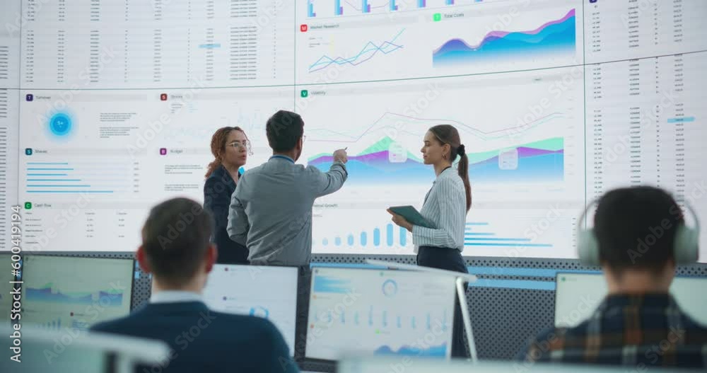 Poster Wide Back Shot of Diverse Team of Financial Analysts Having A Meeting in front of Big Digital Screen With Data In Monitoring Room. Multiethnic Employees Working On Desktop Computers For AI Company.