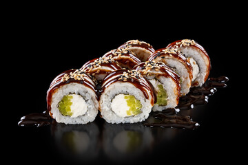 Closeup fresh Sushi Rolls with eel, avocado, cheese philadelphia, sauce unagi and sesame seeds isolated on black background