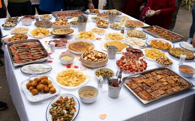 large square table with plates of appetizer food at the inauguration in a village, around unrecognisable people of all ages and ages snacking, popular festival
