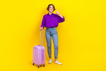 Full length photo of cute confident woman dressed purple shirt showing thumb up holding luggage isolated yellow color background