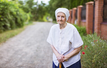 Aged woman standing outdoors near her village house and looking at camera