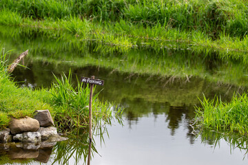 No fishing sign in river with lush green riverbank