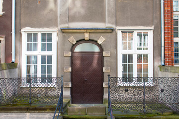 View of the old classic round door on the facade of the building with two tall windows in a white frame and a wrought-iron fence. Brown and grey tones. Poland, Gdansk, April 2023