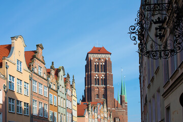 View of the tower of the old Catholic church and ancient buildings against the blue sky. Metal emblem in the foreground. Old architecture. Cityscape. Poland, Gdansk, April 2023