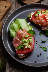 Black bread sandwich with salted salmon, cream cheese, tomato and cucumber in a plate