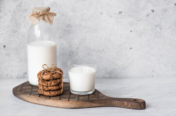 A glass bottle of milk, oatmeal, a stack of Oatmeal cookies and a glass of milk on a stylish wooden board on a concrete table. Rustic style