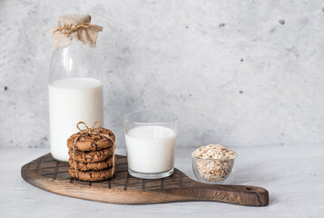 A glass bottle of milk, oatmeal, a stack of Oatmeal cookies and a glass of milk on a stylish wooden board on a concrete table. Rustic style