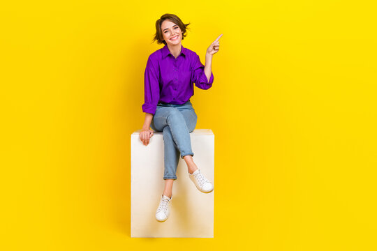 Full body size cadre of young satisfied business promoter lady sit podium point finger novelty brand name isolated on yellow background