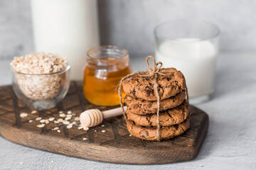 Organic natural cow's milk in a glass bottle, oatmeal, honey and oatmeal cookies on a stylish wooden board on a stone table. Natural eco-friendly products.